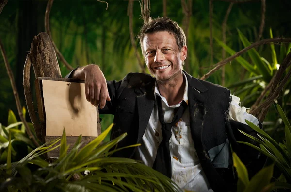 Survivor businessman leaning to a sign in the jungle — Stock Photo, Image