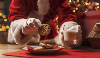 Noel Baba lezzetli bir atıştırmalık yiyor, kurabiye yiyor ve süt içiyor, Noel ve tatil konsepti.