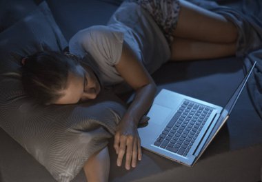 Yorgun bir kadın yatağında dizüstü bilgisayarının önünde uyuyakalıyor.