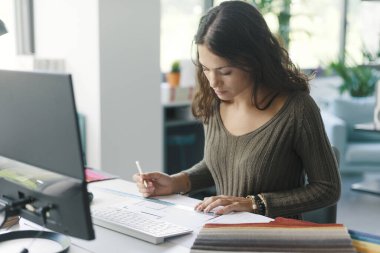 Stüdyosunda çalışan profesyonel bir iç mimar. Masasında oturuyor ve bir proje üzerinde çalışıyor.