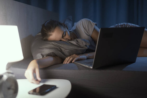 Уставшая женщина лежит в постели и засыпает перед ноутбуком