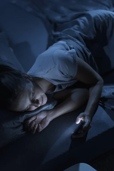 ベッドに寝そべっている笑顔の女性は眠ることができず 彼女はスマートフォンでオンライン接続しています — ストック写真