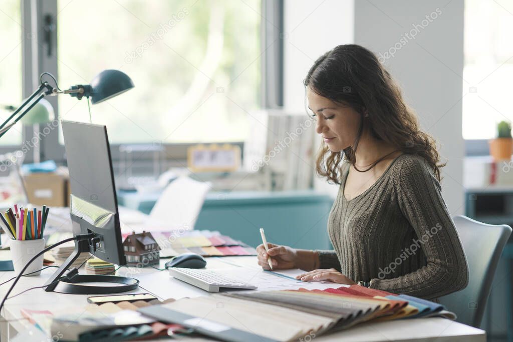 Professional interior designer working in her studio, she is sitting at desk and working on a project