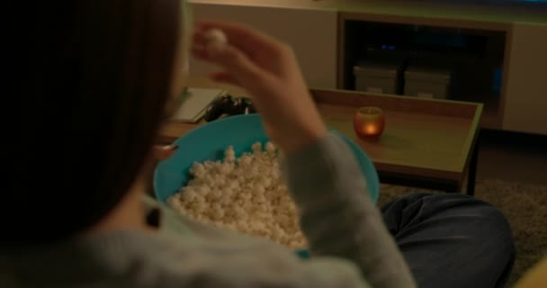 Молодая женщина ест попкорн и смотрит телевизор — стоковое видео