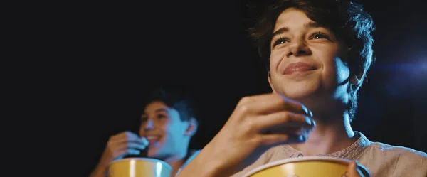 Boy watching a comedy movie at the cinema, he is eating popcorn and smiling