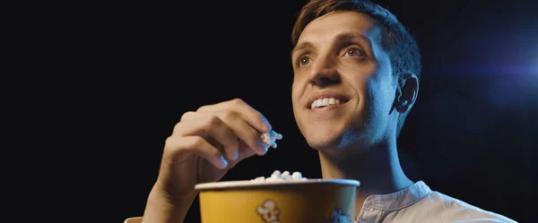 Smiling man watching a movie and eating popcorn, entertainment concept