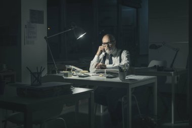 Yorgun şirket işadamı gece geç saatlere kadar çalışıyor, ofiste bir telefon görüşmesi yapıyor.