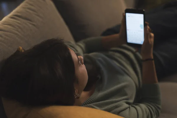 家でリラックスした女の子 彼女はソファに横になって 彼女のスマートフォンでオンライン接続しています — ストック写真