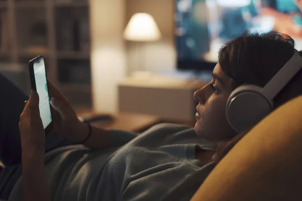 Oturma Odasındaki Kanepede Dinlenen Genç Kulaklık Takıyor Akıllı Telefonuyla Internete — Stok fotoğraf