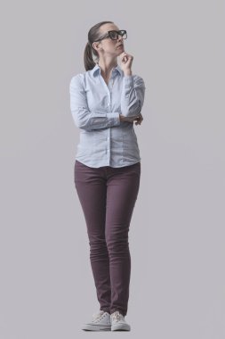 Genç bir kadın eli çenesinde poz veriyor ve düşünüyor. Gri arka planda izole edilmiş.