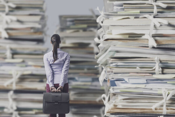 Разочарованная потерянная деловая женщина, уставившаяся на огромные груды бумажной работы, перегрузки на работе и концепцию бюрократии