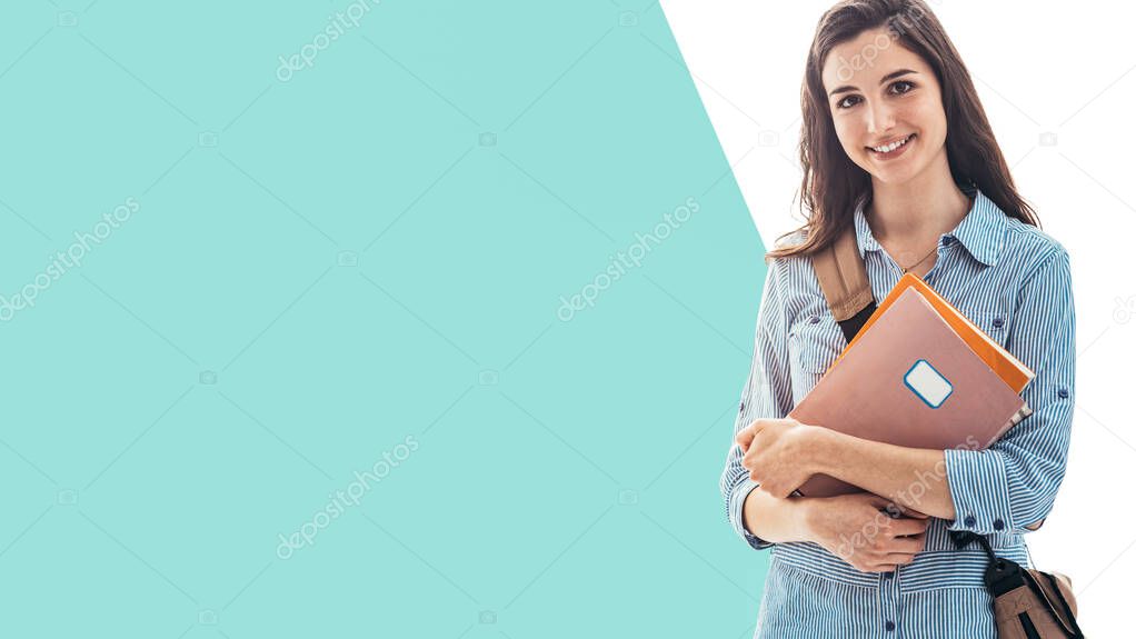 Young female college student portrait, she is smiling at camera and holding books, school and education concept, blank copy space