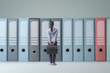 Arşiv, veri yönetimi ve depolama kavramındaki büyük halka klasörlerinin önünde duran kafası karışmış iş kadını