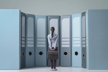 Arşiv, veri yönetimi ve depolama kavramındaki büyük halka klasörlerinin önünde duran kafası karışmış iş kadını