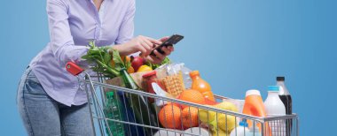 Bir kadın alışveriş arabasına yaslanıyor ve akıllı telefonunu kullanıyor, boş fotokopi alanı