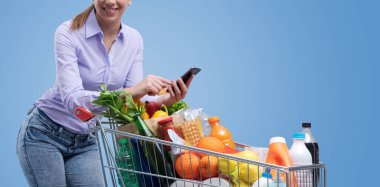 Bir kadın alışveriş arabasına yaslanıyor ve akıllı telefonunu kullanıyor, boş fotokopi alanı