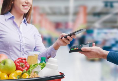 Akıllı telefonuyla market alışverişini yapan kadın, mağaza görevlisi bir POS terminali tutuyor.