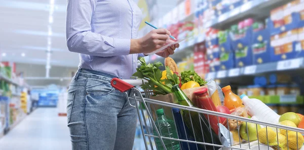 Kobieta Sprawdzająca Listę Zakupów Kupująca Towary Supermarkecie Jej Koszyk Jest — Zdjęcie stockowe