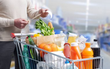 Adam alışveriş arabasının yanında duruyor ve market fişini kontrol ediyor.