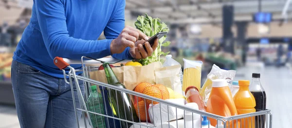 Hombre Haciendo Compras Supermercado Está Empujando Carro Usando Teléfono Inteligente — Foto de Stock