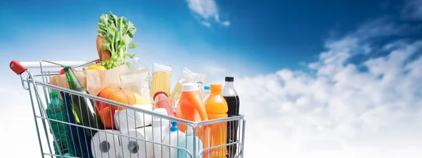 背景に商品と青空が広がるショッピングカート 食料品のショッピングコンセプト — ストック写真
