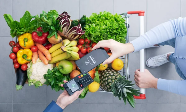 Frau Schiebt Vollen Einkaufswagen Und Bezahlt Lebensmittel Mit Dem Smartphone — Stockfoto