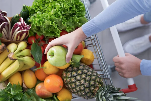 新鮮な野菜や果物でいっぱいのショッピングカートを押す女性 彼女はおいしいリンゴ トップビューを開催しています — ストック写真