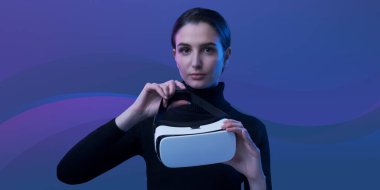 Elinde VR kulaklığı olan çekici genç bir kadın kameraya, sanal gerçekliğe ve yapay deneyim konseptine bakıyor.