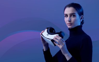 Elinde VR kulaklığı olan çekici genç bir kadın kameraya, sanal gerçekliğe ve yapay deneyim konseptine bakıyor.