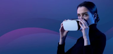 Çekici bir kadın kameraya bakıyor ve yüzüne VR kulaklık tutuyor, sanal gerçeklik deneyimi konsepti.