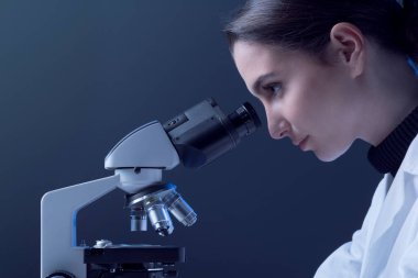 Mikroskopla bakıp örnekleri inceleyen genç araştırmacı, tıbbi araştırma konsepti.