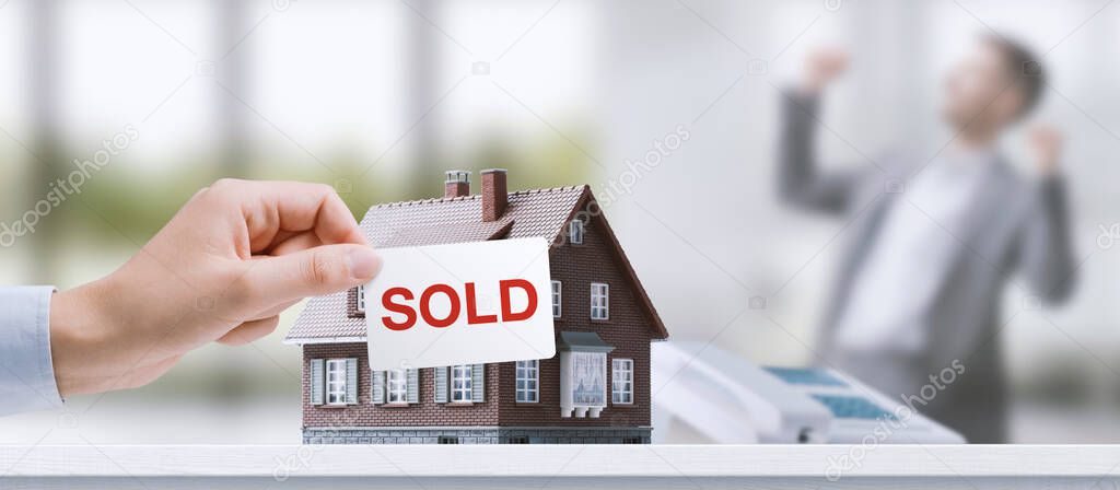 Real estate agent holding a sold sign in front of a model house, successful sale concept