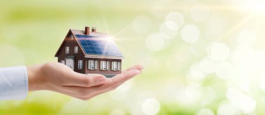 Hand holding an energy efficient model house with solar panels, ecology and sustainability concept clipart