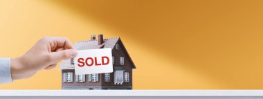 Emlakçı, model bir evin önünde satılan bir tabela tutuyor. Başarılı bir satış konsepti.