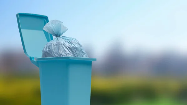 Garbage bag in a trash can and green landscape in the background