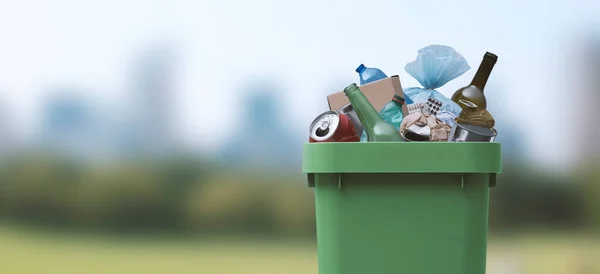 Garbage can full of mixed undifferentiated waste in a park, improper waste management concept