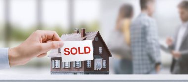 Başarılı ev satışı: bir emlakçı arka planda müşterilerle konuşuyor