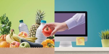 Kadın eli bilgisayar ekranından çıkıyor ve marketten bir domates alıyor. İnternetten alışveriş konsepti.