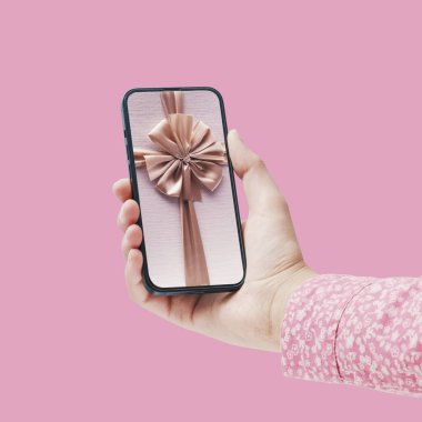 Elinde hediye kurdelesi olan akıllı telefonu olan bir kadın güzel bir sanal hediye alıyor.