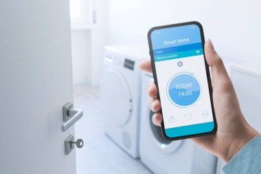 Woman controlling her smart washing machine from her smartphone, she is setting the program using an app