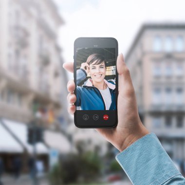 Elinde akıllı telefon ve video olan bir kadın arka planda arkadaşını arıyor.