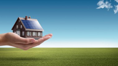 Hand holding an energy efficient model house with solar panels, ecology and sustainability concept clipart