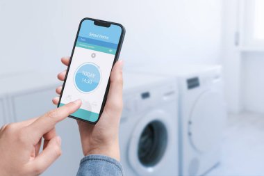 Woman controlling her smart washing machine from her smartphone, she is setting the program using an app