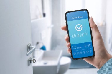 Kadın akıllı telefon kullanarak evinde hava kalitesini kontrol ediyor.