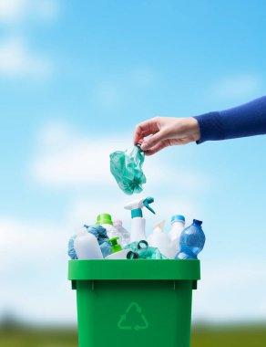 Kadın plastik şişeyi geri dönüşüm kutusuna koyuyor, atık toplama ve geri dönüşüm konseptini ayırıyor.