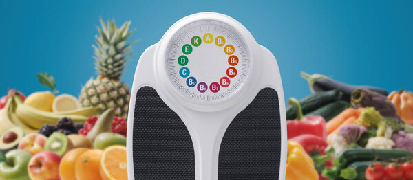 Weight scale with vitamins on the display, lots of fruits and vegetables in the background, healthy diet concept