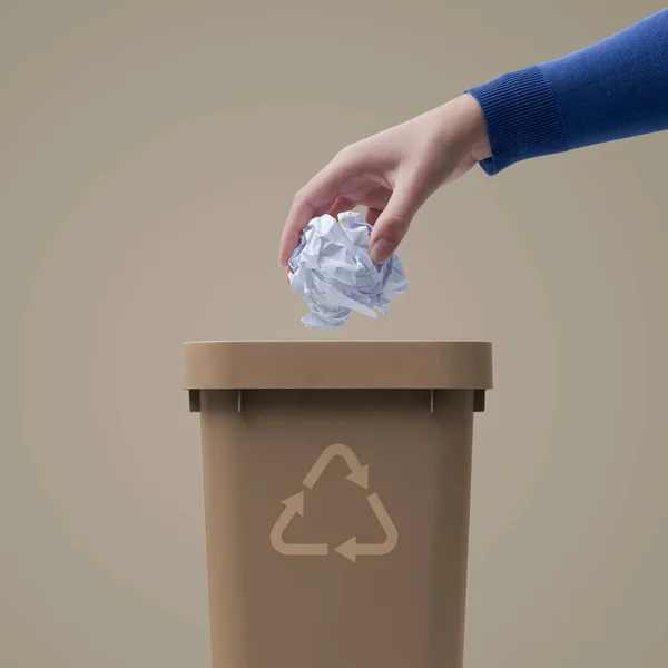 Woman putting crumpled paper in a trash bin, recycling and waste sorting concept