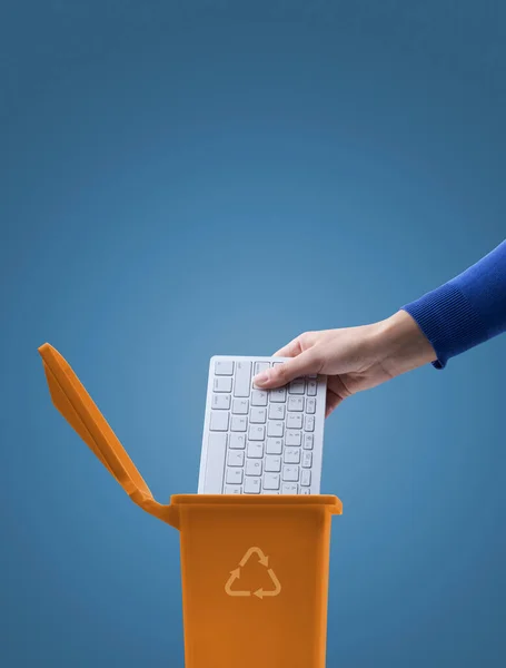 Woman putting a computer keyboard in the e-waste trash bin, recycling concept
