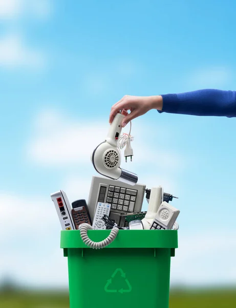 Woman putting an old broken appliance in the trash bin, e-waste and recycling concept