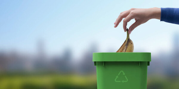 Woman putting biodegradable organic waste in a bin, separate waste collection and recycling concept